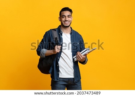 Smart arab guy student with backpack and bunch of books smiling at camera, copy space for advertisement over yellow studio background. Education, university, college, studying, course concept