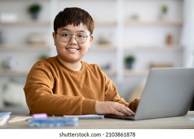 Smart asian chubby teen boy schooler sitting at table in front of modern computer, typing on laptop keyboard, doing homework or having online lesson, studying from home, closeup, copy space