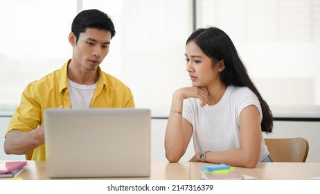 Smart Asian Male Software Engineer Fixing The Online Database Problems On Laptop Computer For Female Marketing Officer In The Office.