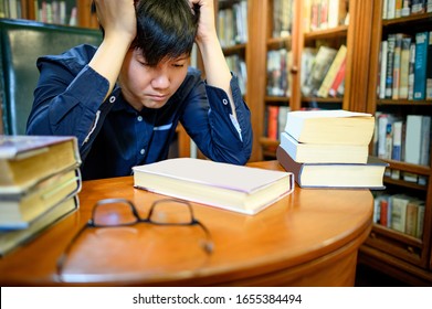Smart Asian man university student feeling stressed and anxious while reading book by vintage bookshelf in college library for education subject and research. Scholarship for education opportunity.