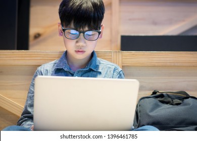 Smart Asian Preteen Boy With Blue Light Blocking Glasses Is Online Learning With His Laptop. Technology And Learning Concept. Homeschooling Anywhere Anytime. Computer Vision Syndrome.