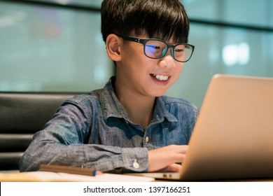 Smart Asian Preteen Boy With Blue Light Blocking Glasses Is Online Learning With His Laptop. Technology And E-learning Concept. Homeschooling Anywhere Anytime. Blue Light From Computer Screen.