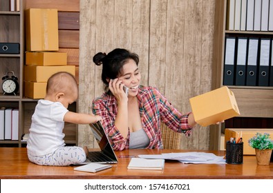 Smart Asian Single Mother Woman Taking Care Baby Multi Task Working At Home Using Laptop,smartphone Packing Products Cardboard, Small Business Startup Entrepreneur, Freelance Lifestyle Shopping Online