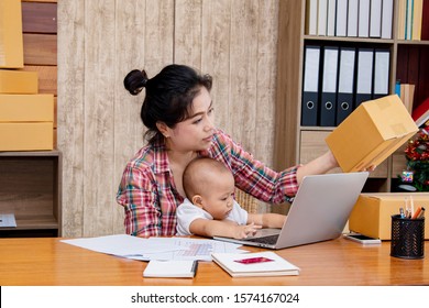 Smart Asian Single Mother Woman Taking Care Baby Multi Task Working At Home Using Laptop,smartphone Packing Products Cardboard, Small Business Startup Entrepreneur, Freelance Lifestyle Shopping Online