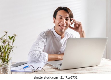 A Smart Asian Young Businessman Sitting At Home Office Pleased Happy Cheerful On Online Working Or Learning Using Laptop Computer Getting A New Job Offer Or Make Good Selling. Work Win Happy Concept.