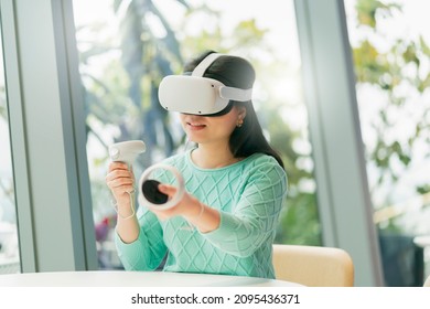 smart attractive asian female business owner weared virtual reality glasses enjoys casual metaverse meeting with concentrate at cafe restaurant,asian female  using oculus rift headset in cafe