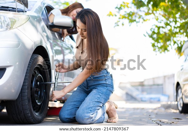 Smart and Attractive Asian woman jacks up her car\
and uses a wrench to change the wheel on a broken car, uses tools\
or equipment, tries to solve problems by self, Car Repairing and\
insurance concept