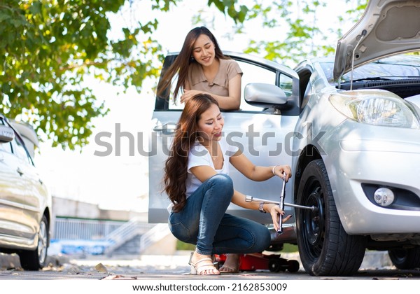 Smart and Attractive Asian woman jacks up her car\
and uses a wrench to change the wheel on a broken car, uses tools\
or equipment, tries to solve problems by self, Car Repairing and\
insurance concept
