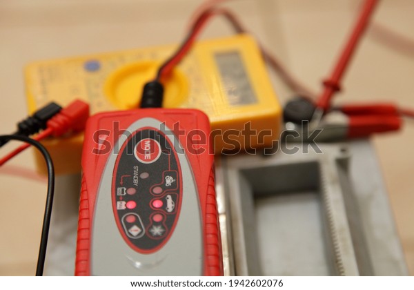Smart automatic\
charger unit on blurred digital multimeter voltmeter and full\
charged Car battery positive pin terminal cleat backgroung closeup,\
plumbic car battery\
charging