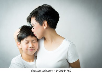 A Smart And Beautiful Asian Mom Gently Kiss Her Preteen Son With Love And Care. Mother And Son Bonding And Love Expression, Mother's Day, Love Mom, Parenting Teen, Single Mom Concept.