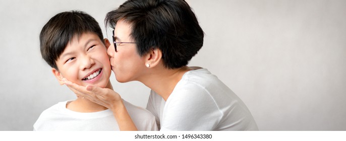 Smart And Beautiful Asian Mom Hold Her Adorable Preteen Son With Love And Kiss. He Smiles With Happiness. Love Expression, Bond, Parenting Teen, Single Mom, Teen Boy And Mom, Mom's Unconditional Love.