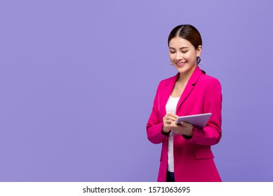 Smart Beautiful Asian Woman In Pink Business Suit Using Digital Tablet Isolated On Purple Background