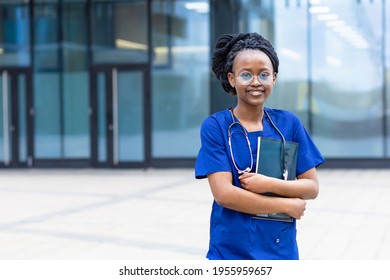 Smart Black Girl Medical Student In Glasses, Happy Young African American Woman Doctor In Blue Uniform, Stethoscope, Smiling Afro Female Nurse With Crossed Hands At University, College, Hospital