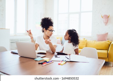 Smart Black Parent Sitting Near Laptop In Bright Room And Talking With Curly Daughter With Tablet In Hands During Break In Freelance Job At Home