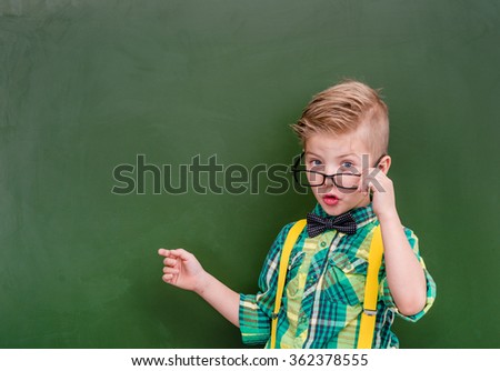 Smart boy points on empty green chalkboard
