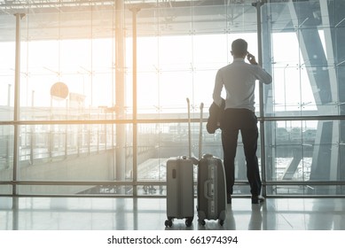 Smart business man standing  in the international airport looking out of building , use telephone ,2 luggages behind him..