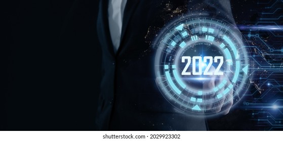 Smart businessman pointing digital dashboard in 2022 on dark blue background. Futuristic technology trend concept. Artificial intelligence (AI), machine learning support for enhancing business growth. - Shutterstock ID 2029923302