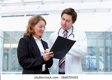 A Smart Businesswoman And A Confident Doctor In A Lab Coat Reviewing Paperwork At The Hospital