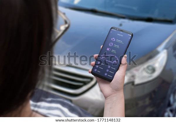 Smart car app\
concept on smart phone in woman hand with car status information.\
Modern car in background