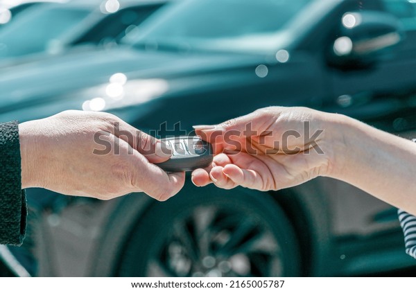 Smart car key on a\
person\'s hand. Hands of a dealer giving car systems key to a female\
buyer outdoors.