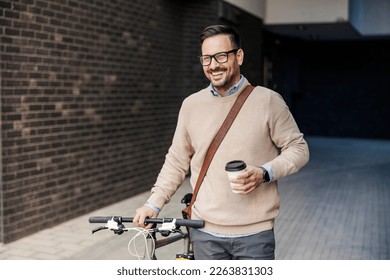 A smart casual businessman in pushing his bicycle on the street and holding coffee to go on his way to work. - Powered by Shutterstock