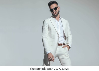 Smart Casual Guy In White Suit With Open Collar Shirt Holding Hand In Pocket And Confidently Posing On Grey Background 