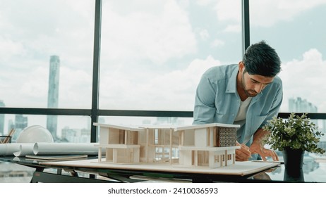 Smart caucasian engineer or project manager measure check, inspect, look at house model while standing near panorama window with city, skyscraper view. Manager design house construction. Tracery