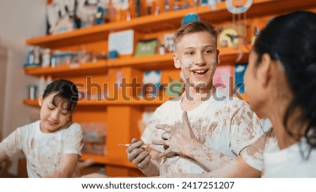 Smart caucasian teenager and happy friend with mixed races put clay on body in art lesson. Diverse highschool student playing and modeling cup of clay at workshop in creative activity. Edification.