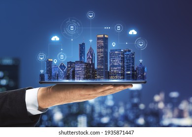 Concepto de ciudad inteligente con diseño de rascacielos reales con brillantes iconos de tecnología digital en la pantalla de tableta digital que llevan mano de hombre de negocios en el fondo borroso de la ciudad de megapolis
