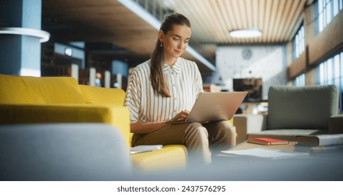 Smart College Student Using Laptop Computer to Study in a Public Library. Beautiful Young Woman Learning Online, Getting Ready for Exams, Taking Notes and Drafting an Essay While Sitting on a Sofa - Powered by Shutterstock