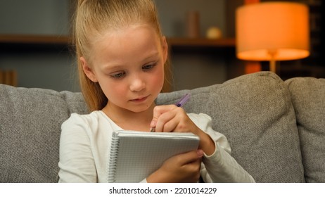 Smart Concentrated Schoolgirl Caucasian Child Primary School Pupil Focused Writing Essay Doing Math Homework Sit On Sofa Making Notes In Notebook Train Calligraphic Handwriting Studying Alone At Home