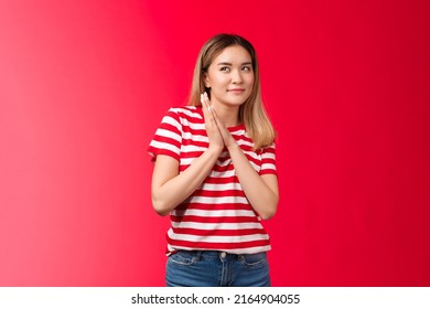 Smart and creative good-looking blond asian girl rubbing palms together devious and cunning have perfect plan, woman smirking curiously look up scheming have idea, stand red background