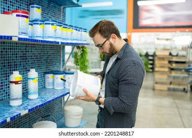 Smart Customer Holding A Bucket Of Paint Or Waterproofer To Look For His Best Option While Shopping At The Hardware Store