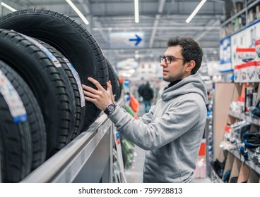 Smart Customer Taking New Tires In The Supermarket For Buying. He Looks Happy. Big Shopping Mall With Car Goods.