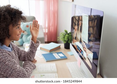 Smart Cute African American Mixed Race Kid Girl Raising Hand Talking With Remote Web Teacher On Social Distance Video Conference Call Elearning Zoom Class On Computer. Children Learning At Home.