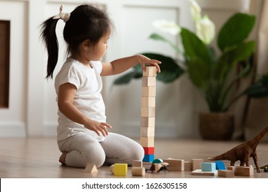 Smart Cute Little Asian Girl Sit On Warm Heated Wooden Home Floor Construct With Building Bricks, Small Vietnamese Child Have Fun Play With Blocks Engaged In Interesting Activity In Living Room