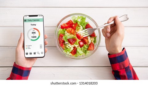 Smart eating and diet planning concept. Man eating vegetable salad and counting calories on mobile application, top view - Shutterstock ID 1314018203