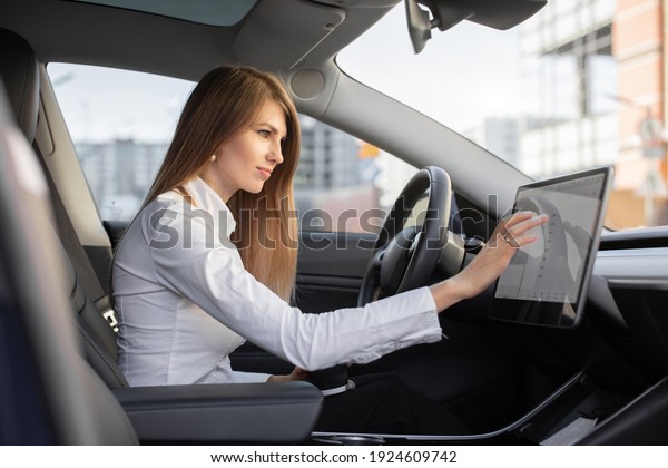 Smart electric car concept.
Pretty woman in formal wear, controlling modern electric
self-steering car with a digital dashboard screen, switching
autopilot mode