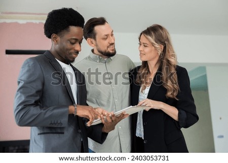 Smart ellegant african american dark skinned real estate in new empty building holding documents of the building showing house to young family couple future ownerships choosing home for family. Stock photo © 
