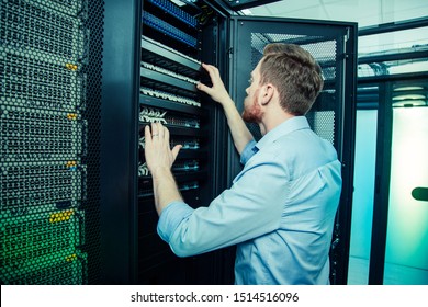 Smart engineer. Nice handsome man looking at the server while trying to fix it