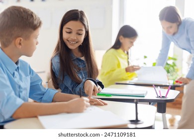 Smart European schoolgirl and boy sitting together at desk in classroom during lesson in private school - Powered by Shutterstock