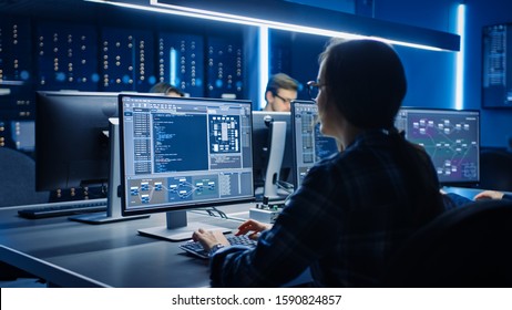 Smart Female IT Programer Working On Desktop Computer In Data Center System Control Room. Team Of Young Professionals Doing Code Programming