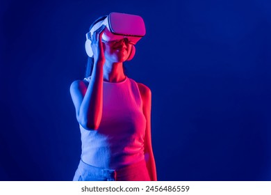 Smart female stand with surrounded by cyberpunk neon light wear VR headset connecting metaverse, futuristic cyberspace community technology. Elegant woman look generated virtual area. Hallucination. - Powered by Shutterstock