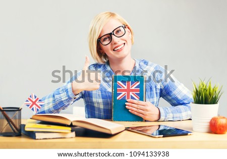 Smart female student, blonde woman wears eyeglasses, holding English language book on table, successful learning concept
