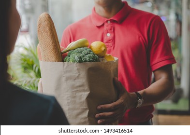 smart food delivery service man in red uniform handing fresh food to recipient and young woman customer receiving order from courier at home, express delivery, food delivery, online shopping concept  - Shutterstock ID 1493416514