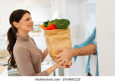 Smart food delivery service man's hands holding paper bag with fresh food. Young woman customer receiving order from courier at home, express food delivery and shopping online concept