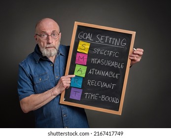 SMART goals ((Specific, Measurable, Attainable, Relevant, Time-bound), Senior man is sharing goal setting methodology on a blackboard. - Shutterstock ID 2167417749