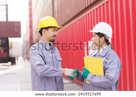 Smart and good looking Asian male and female container yard officers making a handshake together. Team of logistic engineer is working at the container yard.