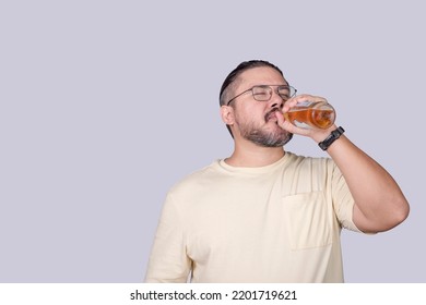 A smart guy in his 30s drinking a bottle of light beer. Savoring the taste. Isolated in a gray background.