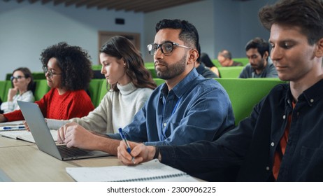 Smart Handsome Male Student Studying in University with Diverse Multiethnic Classmates. Young Man is Using a Laptop Computer to Summarize the Lecture, Study at Home and Pass the Exams - Powered by Shutterstock